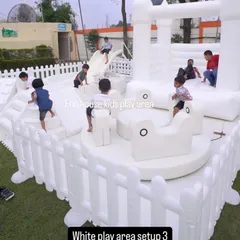Children enjoying our all-white soft play area. This setup includes a bouncy castle, a ball pit with a slide, and a gentle merry-go-round, all designed with safety and modern aesthetics in mind for a chic party experience.