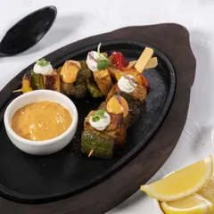 Grilled vegetable skewers served on a hot plate with a side of flavourful dipping sauce. A healthy and delicious vegetarian tapa option.