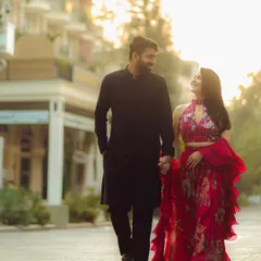 Walking hand-in-hand down a city path at golden hour. The bride's vibrant red outfit pops against the urban background, creating a stunning, romantic image.