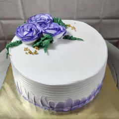 A simple white cake adorned with three beautiful purple buttercream roses and delicate gold sprinkles.