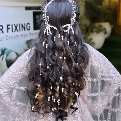 This stunning engagement hairstyle features cascading curls adorned with a beautiful pearl hair accessory. It's a perfect example of a romantic and elegant look for any special occasion.