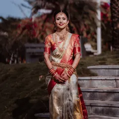 Our bride stands poised and elegant in a classic off-white and red Kanjeevaram saree. The custom blouse, with its intricate sleeve embroidery, perfectly complements this timeless Muhurtham look.
