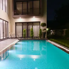 The pool at night, with underwater lights creating a magical glow. The reflection of the home's warm interior lights on the water adds to the serene ambiance.
