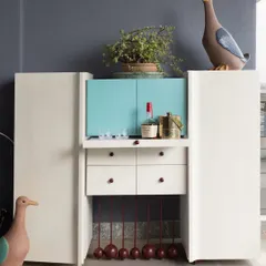 This compact bar cabinet unfolds to reveal a surprisingly spacious interior. The clean white exterior is contrasted with a pop of turquoise inside, complete with drawers and custom holders. The playful, spherical legs add a touch of whimsy to the modern design.