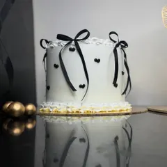 A chic and minimalist cake with black ribbons and tiny hearts. The clean white frosting and simple decorations create a modern and sophisticated look, perfect for a stylish celebration.