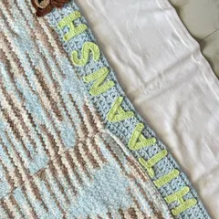 A detailed shot of the personalized name "Hitaansh" and the cute teddy bear appliqué on our knitted cuddle blanket. The letters are crocheted separately and securely stitched on.