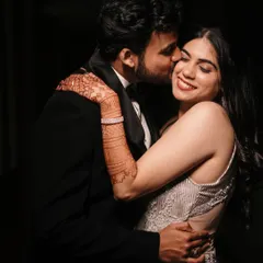 A sweet kiss on the cheek, captured with dramatic, low-key lighting that highlights the emotion and the intricate details of the bride's henna.