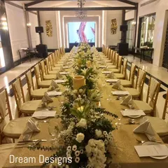 A warm and inviting formal dinner setup. The long table is adorned with a continuous runner of white flowers and greenery, with a large candle centerpiece adding to the intimate and elegant ambiance of the hall.