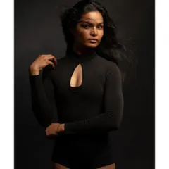 A minimalist and contemplative fine art portrait. The simple black bodysuit and dark background, combined with the motion of the hair, create a sense of quiet introspection.