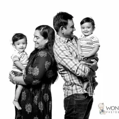 A classic family portrait with a fun twist. Mom and dad stand back-to-back, each holding one of their smiling twin boys, creating a lovely, symmetrical black and white photo.