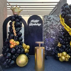 A close-up of the black and gold backdrop, with a neon 'Happy Birthday' sign, a gold plinth for the cake, and a balloon tree topped with a crown.
