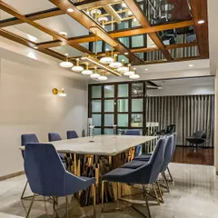 This luxurious dining room features a large marble-topped table with a unique gold base. The blue velvet chairs add a pop of color, and the mirrored ceiling with a modern chandelier creates a sense of grandeur.