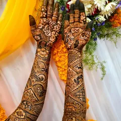Intricate bridal mehndi up to the elbows, set against a festive yellow backdrop. The dark paste promises a beautiful, long-lasting stain, perfect for wedding celebrations.
