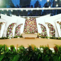 I designed this contemporary outdoor wedding stage with geometric white panels and curved floral arrangements. The central panel is a dense tapestry of flowers, creating a focal point behind the main seating.