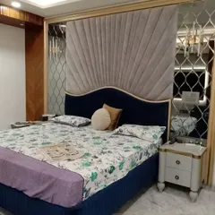 An elegant bedroom design featuring a custom headboard with radiating grey velvet panels and a deep blue base. Mirrored side panels with a geometric lattice design add a touch of glamour and visually expand the space.
