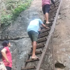 Trekkers climbing a rustic ladder to enter one of the caves. This trek involves some climbing and crawling, making it more adventurous.