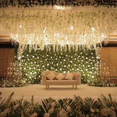 We design stages that serve as the elegant centerpiece for your most important occasions. This sophisticated setup features a lush wall of white and green florals, complemented by a ceiling of cascading wisterias and soft, ambient lighting, perfect for award ceremonies or executive galas.
