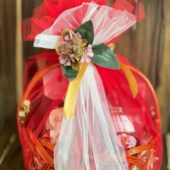 A vibrant corporate farewell gift hamper. The bright red basket is wrapped in red and white net with a floral topper, creating a cheerful and memorable goodbye gift.
