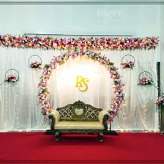 A modern reception stage featuring a large floral ring as the central element, personalized with the couple's initials. The backdrop of white drapes with fairy lights adds a touch of romance and sophistication.