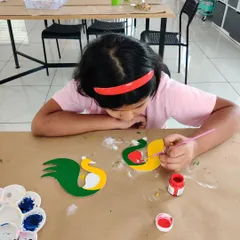 The creative process in action! Here, a young artist is painting the wooden peacock bases, getting them ready for the next step of adding sparkling embellishments.