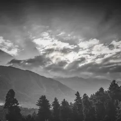 Dramatic clouds pass over layers of mountains and forests. In monochrome, the textures and contrast are heightened, making the landscape feel more expressive and powerful.