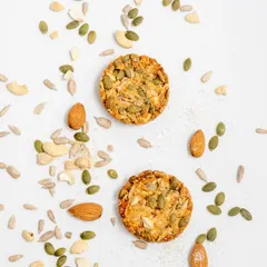 An artistic shot of our multi-seed cookies, surrounded by the raw ingredients we use. You can see the quality of the almonds, cashews, and various seeds that go into every batch.