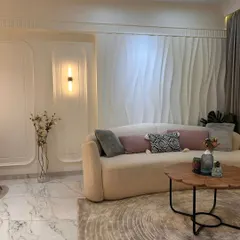 A different angle of the minimalist living room, showing the beautiful marble flooring and the way the curved sofa softens the space. The tall vase with flowers adds a touch of nature and elegance.