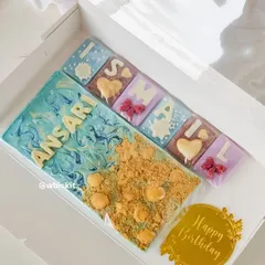 A custom beach-themed chocolate bar and smaller initial chocolates, made for a special birthday. The wave effect and biscuit "sand" create a fun, edible scene.