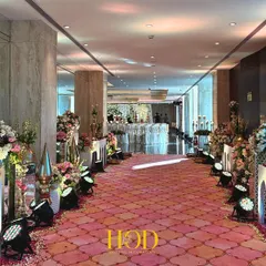A long, dramatic walkway lined with traditional brass vessels, floral arrangements, and a patterned carpet, guiding guests through a journey of color and culture.