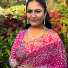 A portrait of the daughter, Supriya, looking radiant in a pink bandhani saree. Her makeup is fresh and glowing, with a sleek ponytail and diamond jewellery for a modern touch.