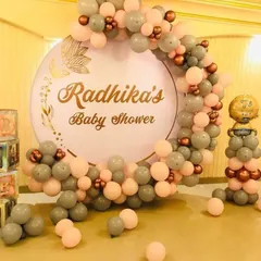 An elegant baby shower for "Radhika." This decoration includes a personalized circular backdrop and a balloon arch in muted tones of grey and peach.