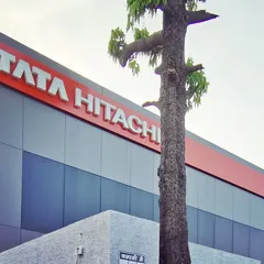 A close-up of the Tata Hitachi facade, showing the clean lines of the ACP rainscreen system and the prominent company branding. The design preserves an existing tree, integrating it thoughtfully into the building's frontage.