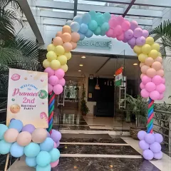 A beautiful pastel rainbow balloon arch at the entrance to a clubhouse for a 2nd birthday party. It's a cheerful and inviting way to greet guests.
