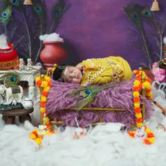 A sleeping newborn Kanha, peacefully resting on a miniature bed. This photo highlights the intricate details of the setup, from the peacock feathers to the garlands.