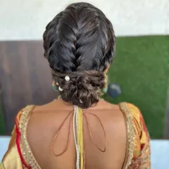 An elegant and intricate updo. This hairstyle features a combination of a fishtail braid and a low bun, accented with small pearls for a touch of classic charm.