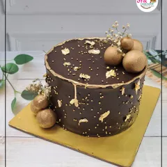 A sophisticated take on a chocolate cake. This design features a smooth chocolate ganache, gold leaf flakes, and golden chocolate spheres for a touch of elegance.