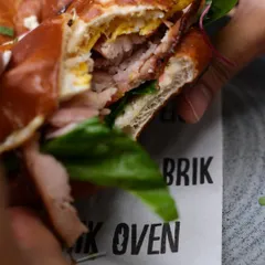 A look inside our hearty pretzel bagel sandwich. You can see the layers of flavor, from the perfectly cooked egg to the fresh greens and meat, all held together by that chewy bagel.