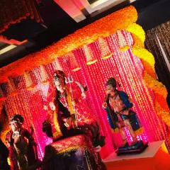 A powerful and traditional setup for a Mata ki Chowki celebration. The decor features a vibrant backdrop of red fabric and stringed flowers, framed by an arch of fresh orange marigolds to create a divine atmosphere.