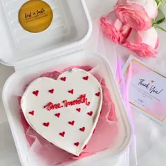 Simple, sweet, and perfect for anniversaries. This heart-shaped bento cake celebrates a one-month milestone with clean red piping and tiny hearts on a smooth white buttercream canvas, presented with fresh roses.