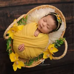 A classic overhead shot of a newborn sleeping peacefully in a basket. The yellow wrap and flowers create a bright and cheerful theme.