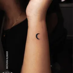 A tiny, solid black crescent moon tattoo on the wrist. This is a perfect example of a minimalist tattoo that is both simple and beautiful.