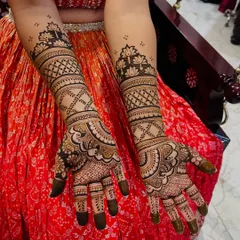 A beautiful example of full-coverage mehendi against a vibrant lehenga. The design features classic paisleys on the palm and delicate lotus motifs at the top.