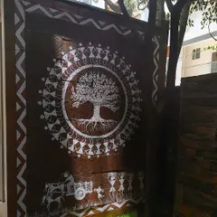 A closer view of the Tree of Life mural. This angle shows the detail in the tree's roots and branches, as well as the ring of dancing figures that encircle it, a classic element of Warli tribal art.