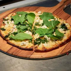 A freshly baked pizza on a wooden peel, ready to be served. The simple yet delicious combination of greens and cheese is a testament to our focus on quality and flavour.