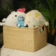 This rectangular woven basket is shown as a charming storage solution for soft toys and cushions. Its durable construction and cut-out handles make it a practical and safe choice for a child's room or living area.