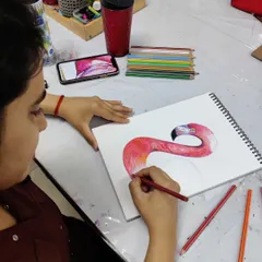 Another angle of the student working on her flamingo drawing, showing the layering of different shades of red and pink to build up color depth.