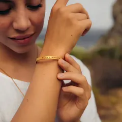 A woman adjusts a delicate gold cuff on her wrist, engraved with the coordinates of a special place. It's a subtle, meaningful way to carry a cherished memory with you always.