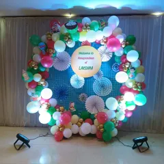 A colorful and festive decoration for the Annaprashan of Lakshya. This circular backdrop uses a net design, paper fans, and a multi-colored balloon garland to create a joyful atmosphere for the baby's first meal ceremony.