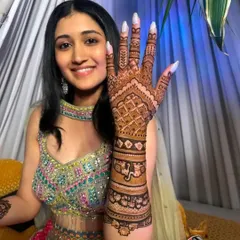 A joyful bride from her mehandi ceremony, holding up her hand to give a clear view of the detailed henna art we created for her.