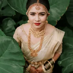 A striking bridal portrait where the bride, in her traditional gold and cream saree, is framed by lush green leaves. We use natural elements to create artistic and memorable portraits that highlight the bride's elegance and personality.